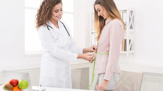 Médica midiendo el perímetro abdominal de una paciente para evaluar el IMC antes de una cirugía de la obesidad